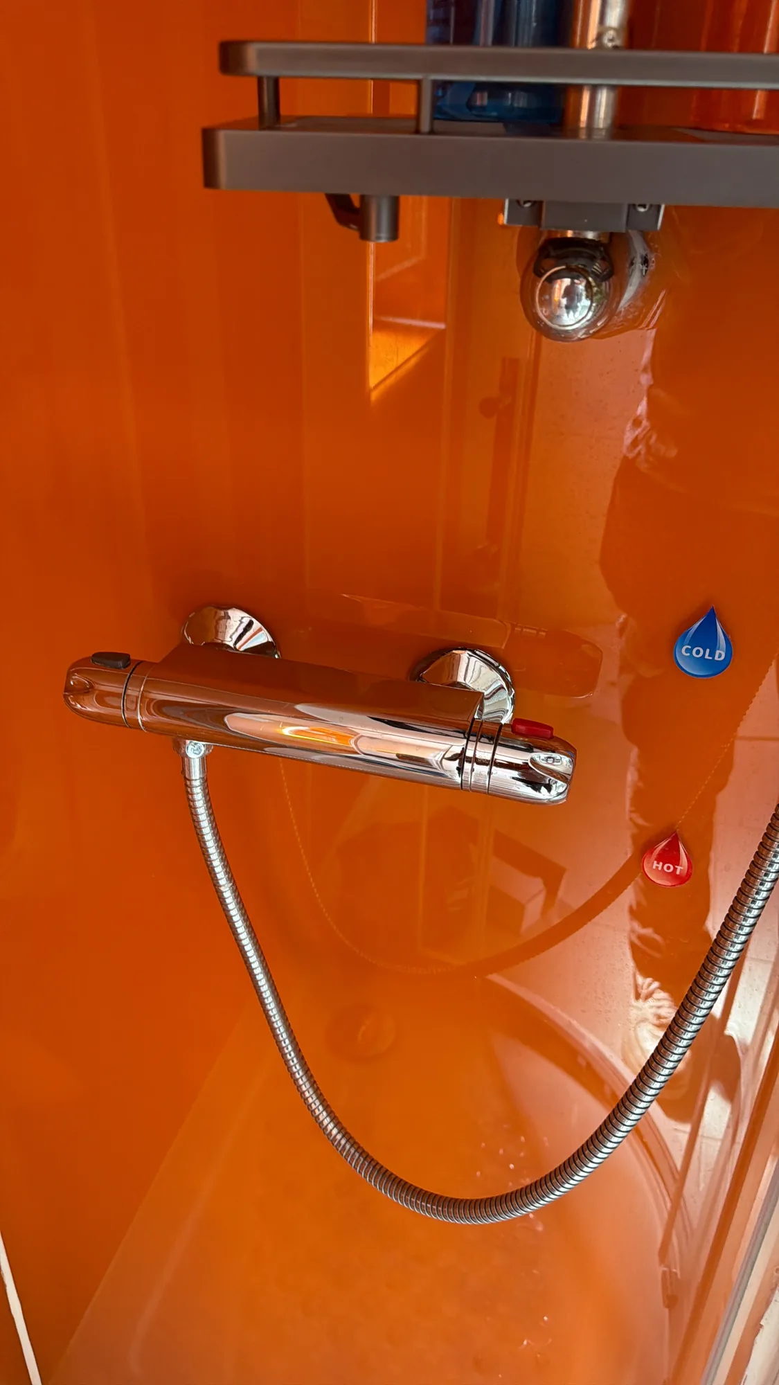 A chrome thermostatic shower mixer valve fitted against a bright orange shower panel.