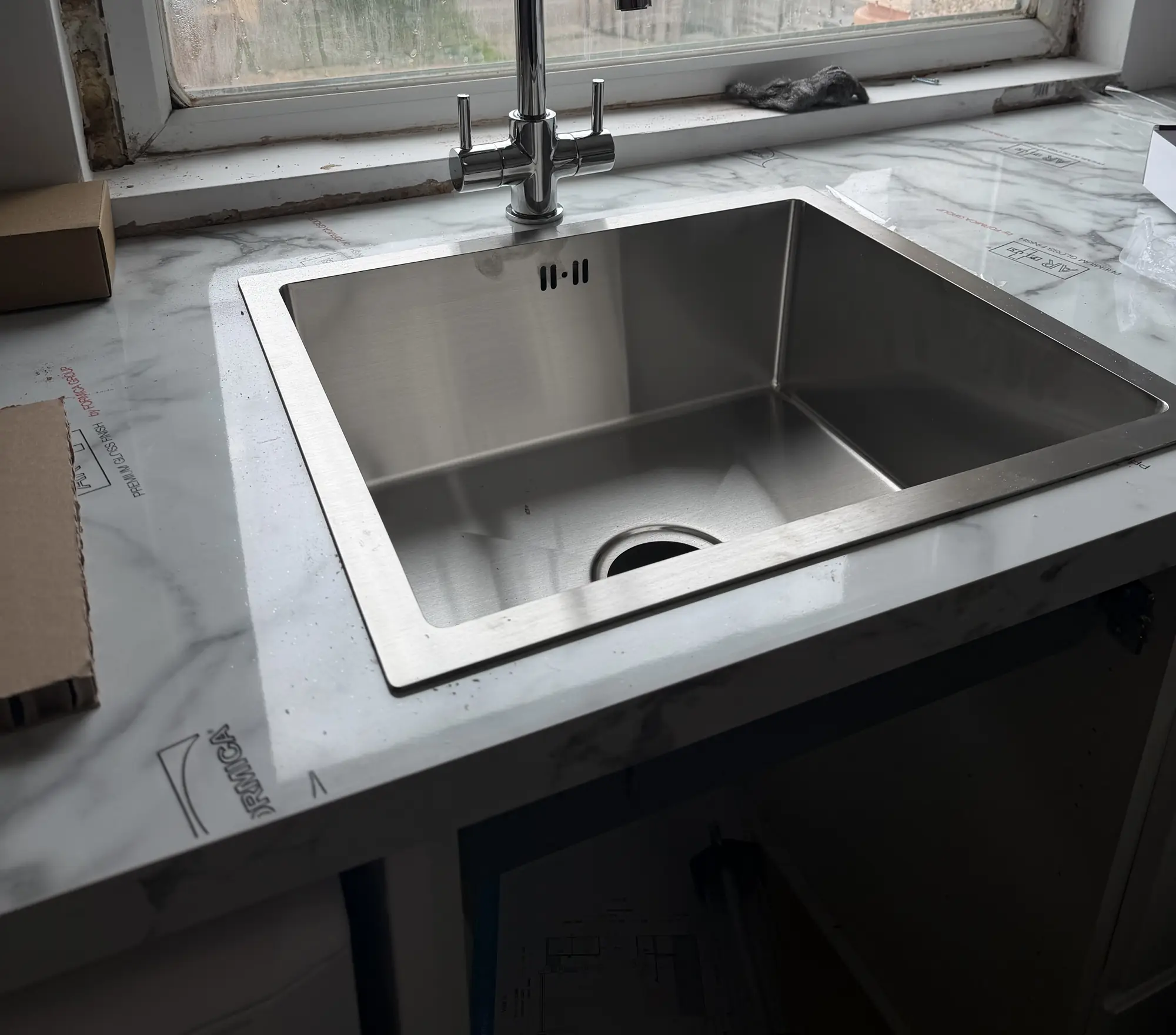 A new stainless steel sink and chrome mixer tap installed in a marble effect kitchen worktop.
