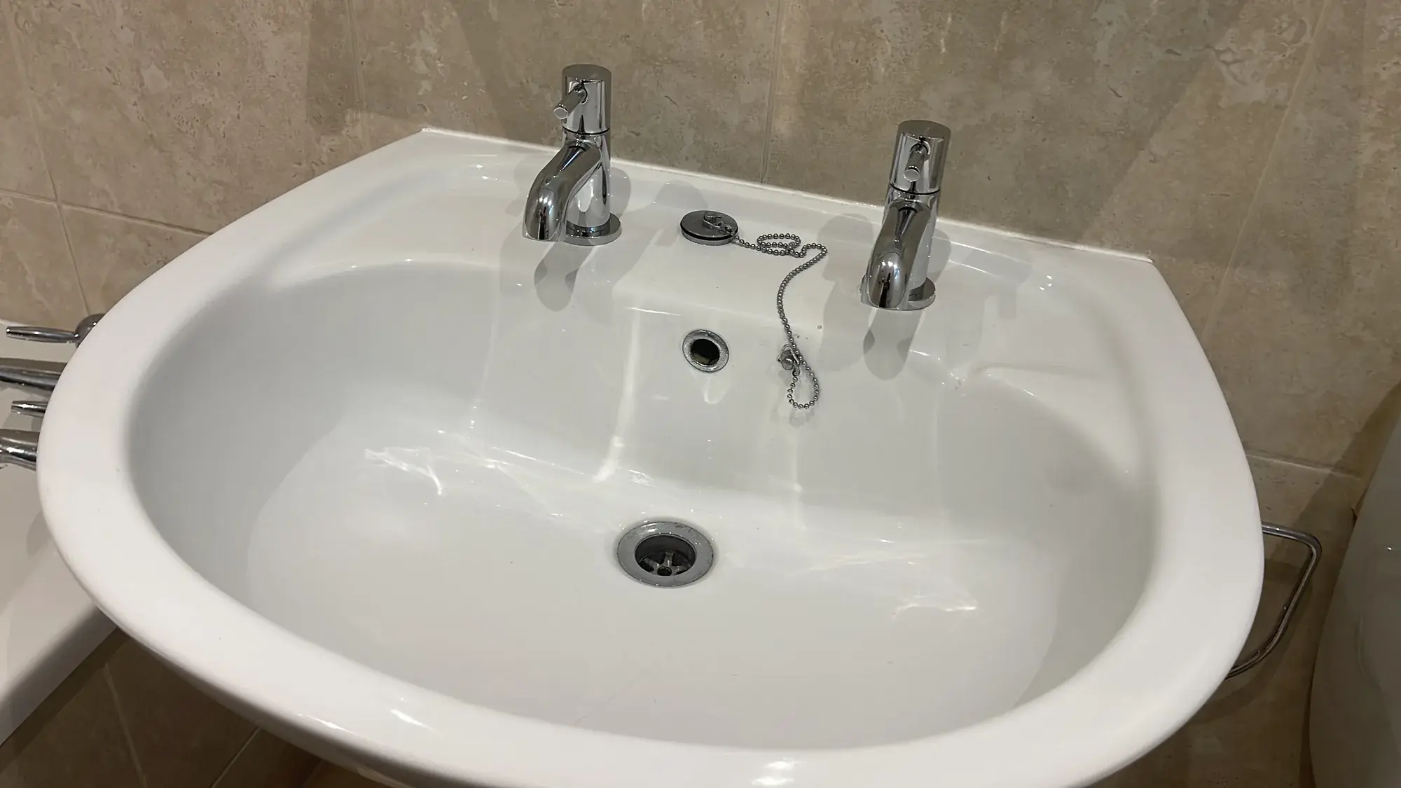 A white bathroom basin fitted with a pair of chrome pillar taps and a chrome waste.