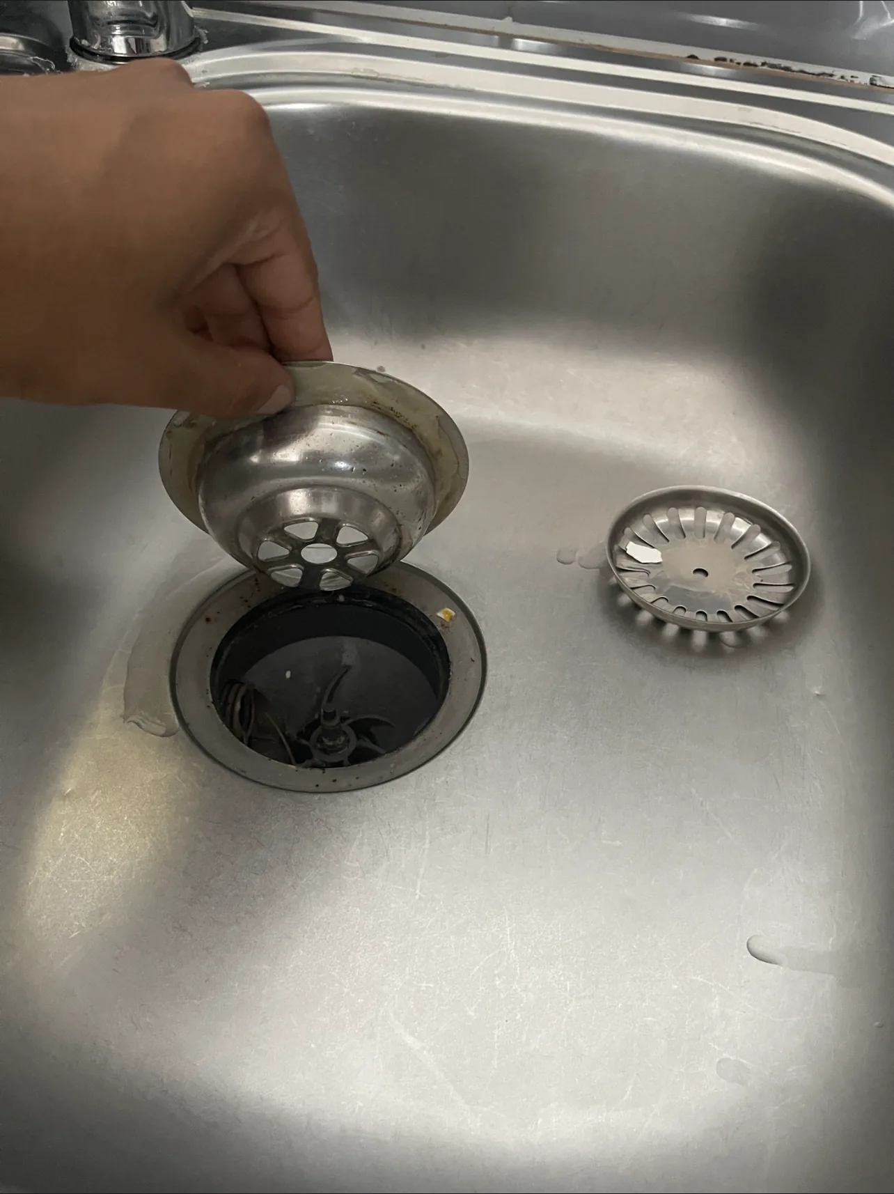 A strainer basket lifted out of a kitchen sink waste while the waste is checked.